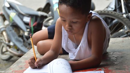 Le jeune Daniel Cabrera, en train de faire ses devoirs sur un trottoir &agrave; Mandaue City (Philippines).&nbsp; (STR / AFP)