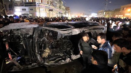 Passers-by in front of the wreckage of a vehicle destroyed by a drone strike, February 7, 2024 in Baghdad (Iraq).  (MURTADHA AL-SUDANI / ANADOLU / AFP)