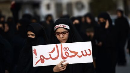 A Bahreïn, une femme manifeste dans le village de Jidhafs, à l'ouest de Manama, la capitale, contre l'exécution de l'important dignitaire religieux chiite Nimr al-Nimr par les autorités saoudiennes , le 2 Janvier 2016. Bahreïn compte une majorité de chiites comme la région d'Arabie saoudite, riche en pétrole, où le religieux exécuté a été un moteur dans les manifestations qui ont éclaté en 2011 pour protester contre ce que les chiites considèrent comme leur marginalisation dans le royaume. Sur le panneau on peut lire : «soyez damnés» . (MOHAMMED AL-SHAIKH / AFP)