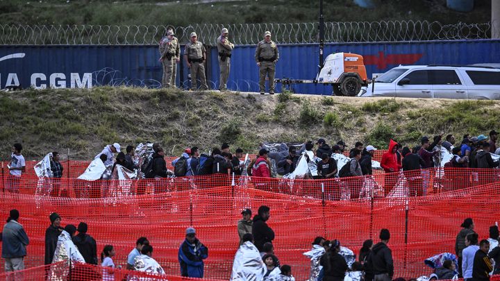 Des policiers américains surveillent des personnes attendant de passer la frontière entre le Mexique et les Etats-Unis, le 22 décembre 2023, à Eagle Pass, au Texas. (CHANDAN KHANNA / AFP)