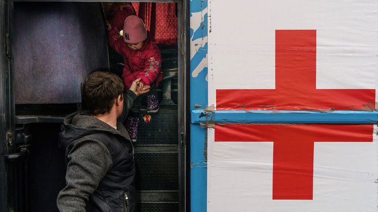 Un volontaire aide un enfant à descendre d'un bus de la Croix-Rouge, le 1er avril à Zaporijié, en Ukraine. Une équipe du CICR tente toujours d'accéder à Marioupol pour évacuer les civils bombardés par l'armée russe. (EMRE CAYLAK / AFP)