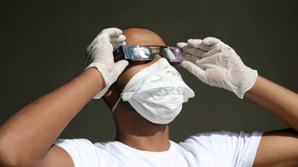 Cet homme&nbsp;observe&nbsp;le phénomène astronomique à Riyad (Arabie Saoudite), en respectant&nbsp;toutes les recommandations des autorités sanitaires : le port du masque, en raison de la pandémie de Covid-19, et le port de lunettes, pour l'éclipse. (AHMED YOSRI / REUTERS)