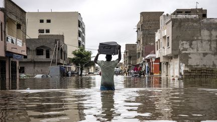 Un homme porte une valise alors qu'il déplace ses affaires hors de sa maison dans le quartier inondé de Keur Massar, à Dakar, le 20 août 2021. (JOHN WESSELS / AFP)