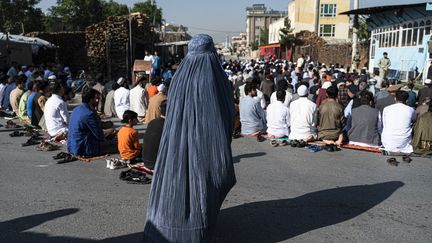 Une femme afghane derrière des fidèles musulmans en pleine prière, le 1er mai 2022, à Kaboul, en Afghanistan. (WAKIL KOHSAR / AFP)