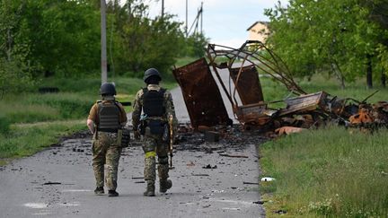 Des soldats ukrainiens marchent à côté d'un véhicule militaire détruit dans le village de&nbsp;Rus'ka Lozova, au nord de Kharkiv (Ukraine), le 28 mai 2022. (GENYA SAVILOV / AFP)