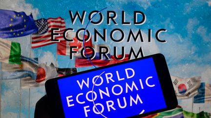 Le logo du Forum économique mondial est affiché sur un smartphone, avec le Forum économique mondial visible en arrière-plan, sur cette photo d'illustration prise à Bruxelles, en Belgique, le 14 janvier 2024. (JONATHAN RAA / NURPHOTO / AFP)