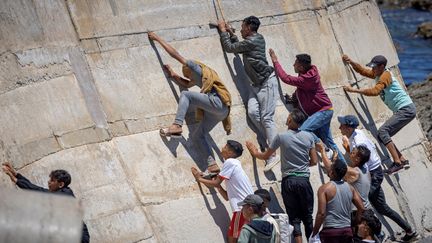 Des migrants escaladent une digue dans la ville nordique de Fnideq après avoir tenté de traverser la frontière entre le Maroc et l'enclave nord-africaine espagnole de Ceuta, le 19 mai 2021. (FADEL SENNA / AFP)