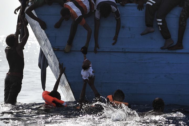 Des migrants tentent de protéger&nbsp;un enfant suspendu au-dessus de l'eau au large des côtes libyennes, le 4 octobre 2016.&nbsp; (ARIS MESSINIS / AFP)