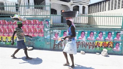 Des Haïtiens passent devant des affiches des deux candidats au deuxième tour de la présidentielle (19 mars) (AFP / Thony Belizaire)