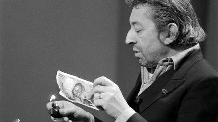 Serge Gainsbourg s'apprête à mettre le feu à un "Pascal" (billet de 500 francs) le 11 mars 1984 sur le plateau de l'émission "7 sur 7", à Paris (PHILIPPE WOJAZER / AFP)