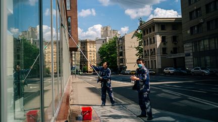 Deux hommes, dont l'un masqué, lavent la vitrine d'un commerce, à Moscou, le 28 mai 2020. (DIMITAR DILKOFF / AFP)