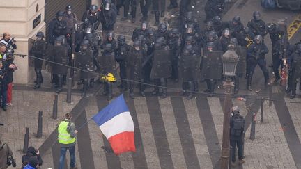 Un homme tient un drapeau tient un drapeau tricole face aux forces de l'ordre, près des Champs-Elysées à Paris, dans la matinée du 8 décembre. (LUCAS BARIOULET / AFP)