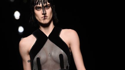 Ici quasi toutes les pièces de la collection d'Alexander Wang étaient noires, avec force clous argentés partout. Ils envahissaient les cols roulés, dessinaient le bas des pantalons, rehaussaient les plastrons de pulls zippés et soulignaient les emmanchures des robes. Même les franges d'une longue jupe noire asymétrique n'échappaient pas au métal, qui s'invitait aussi sur les torsades d'un pull blanc porté sur un jean bleu, rare touche colorée dans cet océan de noirceur, avec une parka écossaise, rouge et noire. Les fines chaînes s'invitaient entre les poches zippées d'une petite veste à triple boutonnage, des blousons et manteaux lamés aux épaules de fourrure surdimensionnées réchauffaient des robes et jupes en maille transparentes.
 (JEWEL SAMAD / AFP)