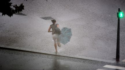 Une femme tente de se mettre à l'abri de la pluie lors d'un orage à Lyon, en septembre 2008. (JEAN-PHILIPPE KSIAZEK / AFP)