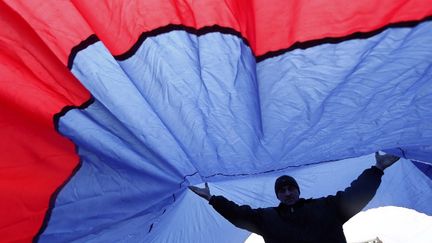 Un homme aide &agrave; porter un drapeau russe g&eacute;ant, le 27 f&eacute;vrier 2014, lors d'une manifestation devant le Parlement de Crim&eacute;e, &agrave; Simferopol (Ukraine). (BULENT DORUK / ANADOLU AGENCY / AFP)