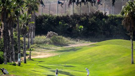 Des personnes jouent au golf tandis que, derri&egrave;re eux, des migrants qui ont tent&eacute; de traverser la fronti&egrave;re entre le Maroc et l'Espagne sont arr&ecirc;t&eacute;s par la police, &agrave; Melilla (Espagne), le 22 octobre 2014. (REUTERS)