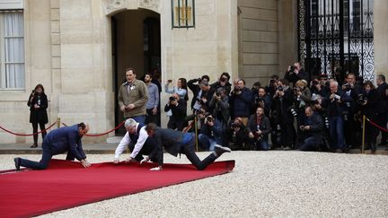 Sous l'oeil des photographes, trois employés s'activent à dérouler le tapis rouge avant l'arrivée d'Emmanuel Macron. (NICOLAS TAVERNIER / REA)