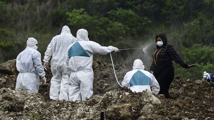 Une&nbsp;équipe envoie&nbsp;du produit désinfectant sur&nbsp;une femme,&nbsp;lors de l'enterrement d'une victime présumée du coronavirus dans un cimetière de Tegucigalpa (Honduras), le 21 juin 2020. (ORLANDO SIERRA / AFP)