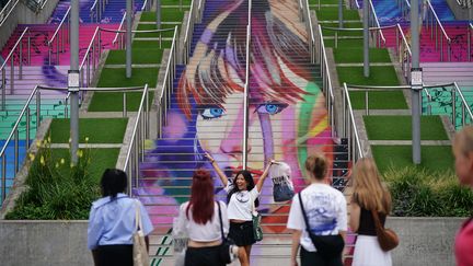 Une "Swiftie", fan de Taylor Swift, se fait photographier devant le portrait de son idole peint sur des escaliers, à Wembley, le 14 août 2024. (YUI MOK / MAXPPP)