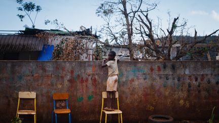 Un jeune Mahorais jette un œil à son école par-dessus le mur, le 19 décembre 2024, après le passage du cyclone Chido sur l'archipel de Mayotte. (DIMITAR DILKOFF / AFP)