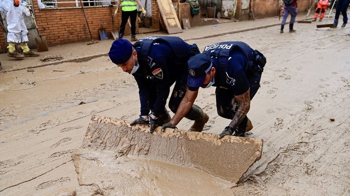 Des policiers espagnols poussent de la boue avec une planche de bois dans les rues d'Alfafar, près de Valence, le 4 novembre 2024. (JOSE JORDAN / AFP)