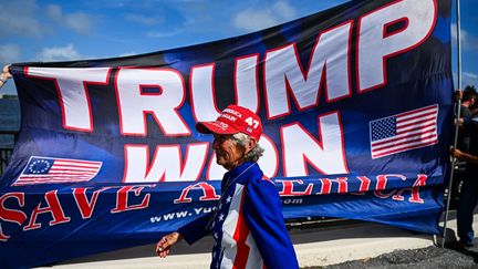 Une partisane de Donald Trump passe devant une banderole soutenant le président républicain, le 6 novembre 2024 à Palm Beach (Floride). (CHANDAN KHANNA / AFP)