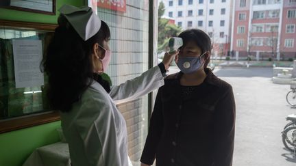 Une soignante prend la température d'une femme à l'entrée d'un hôpital à Pyongyang (Corée du Nord), le 1er avril 2020. (KIM WON JIN / AFP)