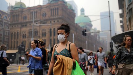 Des habitants de Sydney portent des masques, le 10 décembre 2019, pour se protéger des fumées des feux.&nbsp;Dans la capitale, cette fumée toxique a déclenché des détecteurs de fumée, contraignant les pompiers à aller de bureaux en bureaux, sirènes hurlantes.&nbsp; (STRINGER / REUTERS)