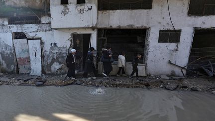 Une famille palestinienne marche au bord d'une rue inondée dans le camp de réfugiés à Tulkarem, où l'armée israélienne a mené des raids nocturnes, le 19 janvier 2024. (ZAIN JAAFAR / AFP)