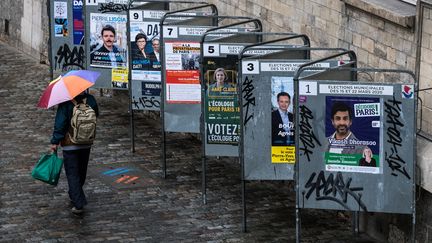 Un homme dépasse en marchant une série d'affiches de campagne électorale, le 14 mars 2020, à Paris. (JOEL SAGET / AFP)