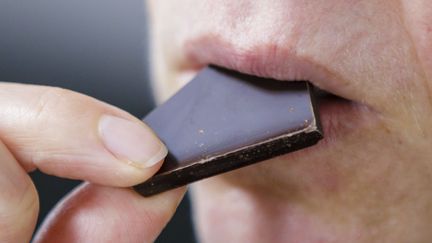 Une femme porte un morceau de chocolat à sa bouche. (THOMAS TRUTSCHEL / PHOTOTHEK)