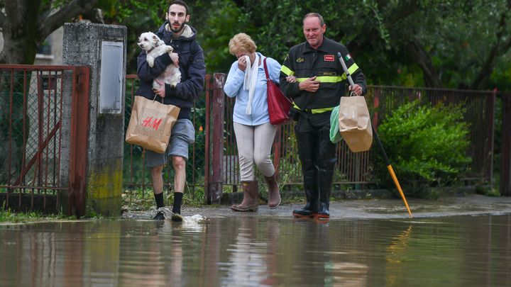 Des pompiers aident une femme, visiblement émue, à évacuer dans une rue inondée à Castel Bolognese, en Italie, le 17 mai 2023. (PIERO CRUCIATTI / ANADOLU AGENCY / AFP)