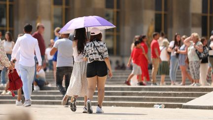 Des passants s'abritent du soleil avec une ombrelle près de la Tour Eiffel, à Paris, le 15 juin 2023. (MOHAMAD ALSAYED / ANADOLU AGENCY / AFP)