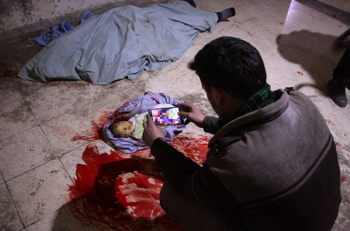 Un homme prend en photo le cadavre de son bébé, dans l'hôpital de Douma, dans l'enclave rebelle de la Ghouta orientale, près de Damas (Syrie), le 19 février 2018. (HAMZA AL-AJWEH / AFP)