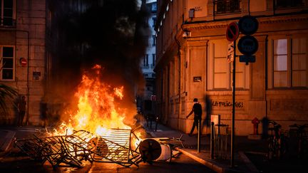 Des barrières de sécurité en feu dans un quartier de Lyon, le 30 juin 2023, où on peut voir sur le mur d'un immeuble l'inscription "La police tue". Des violences urbaines éclatent partout en France durant plusieurs jours après la mort du jeune Nahel, 17 ans, tué par un policier à Nanterre (Hauts-de-Seine), le 27 juin. (JEFF PACHOUD / AFP)