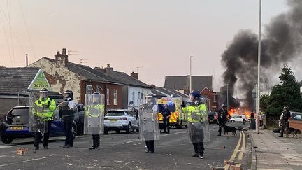 De la fumée s'échappe d'un incendie déclenché par des manifestants alors que la police anti-émeute monte la garde après des troubles près de la mosquée de Southport, dans le nord-ouest de l'Angleterre, le 30 juillet 2024. (ROLAND LLOYD PARRY / AFP)