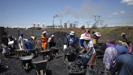 Des Sud-Africaines remplissent des brouettes de charbon dans la région de Johannesburg. Plus au loin, la centrale nucléaire de Duvha, gérée par l'entreprise publique sud-africaine Eskom. Photo prise le 5 février 2015. (MARCO LONGARI / AFP)