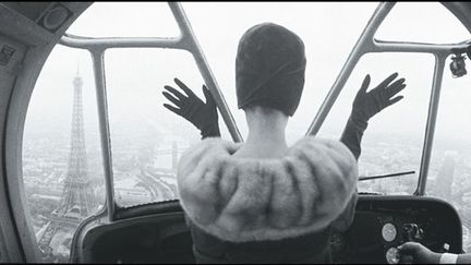 Paris vu d’avion ! Quel bonheur pour une femme chic de s’envoler en portant un chapeau Pierre Cardin. La composition est révolutionnaire et d’un graphisme intemporel. Vue de dos, les mains ouvertes comme pour saisir la ville, la Tour Eiffel en ligne de mire, la nuque bien dégagée, soulignant le port de tête. La pose est si parlante que l’on a l’impression de voir le visage de cette femme, mystérieuse et sophistiquée.
 (Norman Parkinson)