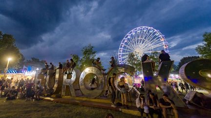 Des festivaliers rassemblés autour de lettres géantes indiquant "Eurocks", avec une grande roue illuminée en arrière-plan, lors de la 33e édition du festival de musique rock des Eurockeennes de Belfort à Sermamagny, dans l'est de la France, le 29 juin 2023. (JEAN-CHRISTOPHE VERHAEGEN / AFP)