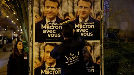 Un militant colle des affiches de campagne d'Emmanuel Macron à Vanves (Hauts-de-Seine), le 16 mars 2022. (LUDOVIC MARIN / AFP)