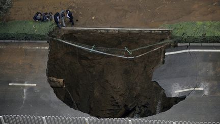 Des curieux observent un trou gigantesque form&eacute; dans la chauss&eacute;e de la ville chinoise de&nbsp;Xi'an, le 27 octobre 2013. Une canalisation d&eacute;fectueuse serait &agrave; l'origine de ce gouffre. (REUTERS)