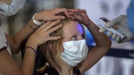 Un employé vérifie la température d'une jeune passagère avant d'embarquer pour un vol pour Paris, à l'aéroport de Tocumen, au Panama, le 11 mai 2020. (LUIS ACOSTA / AFP)