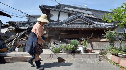 Une femme nettoie devant sa maison, dans la région de Kumamoto (Japon), qui s'est effondrée après un séisme, le 15 avril 2016. (KAZUHIRO NOGI / AFP)