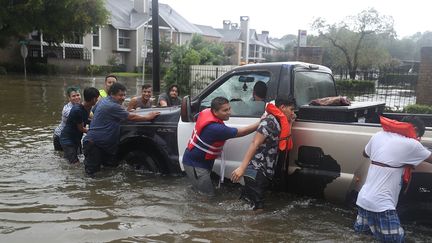 Des habitants de Houston poussent un pick-up dans une rue inondée, le 27 août 2017, après le passage de la tempête Harvey sur le Texas (Etats-Unis). (JOE RAEDLE / GETTY IMAGES NORTH AMERICA / AFP)