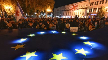 Des manifestants éclairent un drapeau de l'UE lors d'un rassemblement organisé le 20 octobre 2024 à Tbilissi, une semaine avant des élections cruciales pour l'avenir de la Géorgie. (VANO SHLAMOV / AFP)