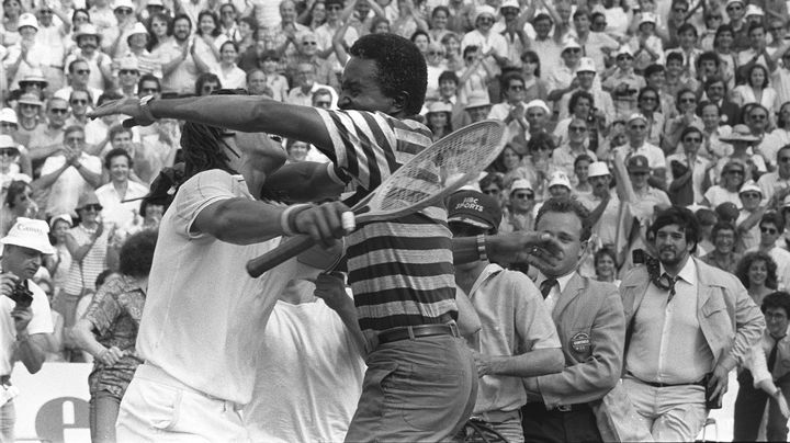 Yannick Noah embrasse son père, Zacharie Noah, sur le court central après avoir remporté le tournoi de tennis de Roland-Garros en battant le Suédois Mats Wilander, le 5 juin 1983. (DOMINIQUE FAGET / AFP)