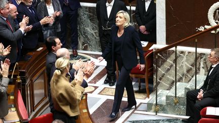 La présidente du Rassemblement national, Marine Le Pen (C), applaudie par son groupe, rejoint son siège après avoir prononcé son discours lors du débat précédant les votes des motions de censure sur le gouvernement du Premier ministre Michel Barnier à l'Assemblée nationale à Paris, le 4 décembre 2024. (ALAIN JOCARD / AFP)