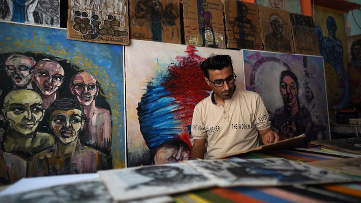 L'artiste palestinien Ahmad Mhanna peint sur du carton provenant des colis d'aide humanitaire, à Deir el-Balah, le 26 juillet 2024. (BASHAR TALEB / AFP)