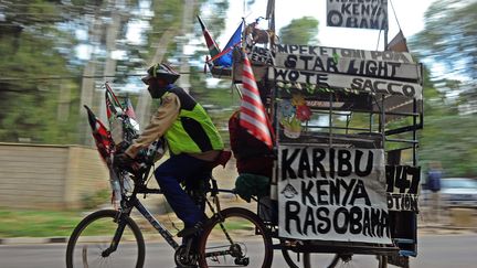 Un vendeur de produits d&eacute;riv&eacute;s se prom&egrave;ne &agrave; v&eacute;lo avec des drapeaux am&eacute;ricains et des pancartes "Bienvenue Obama". Cette visite est consid&eacute;r&eacute;e comme un gros &eacute;v&eacute;nement commercial pour les K&eacute;nyans. (TONY KARUMBA / AFP)