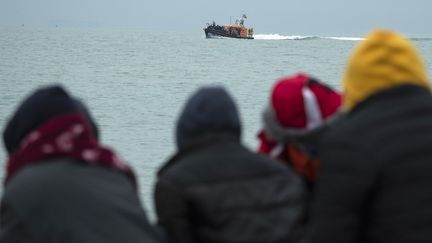 Des personnes&nbsp;assis sur la plage regardent un canot de sauvetage de la RNLI (Royal National Lifeboat Institution) s'approcher d'une plage de Dungeness sur la côte sud-est de l'Angleterre le 24 novembre 2021. (BEN STANSALL / AFP)